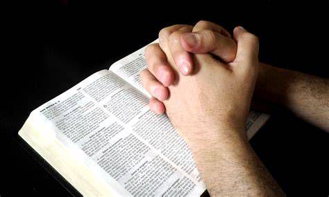 Manos entrelazadas en oración con una Biblia abierta